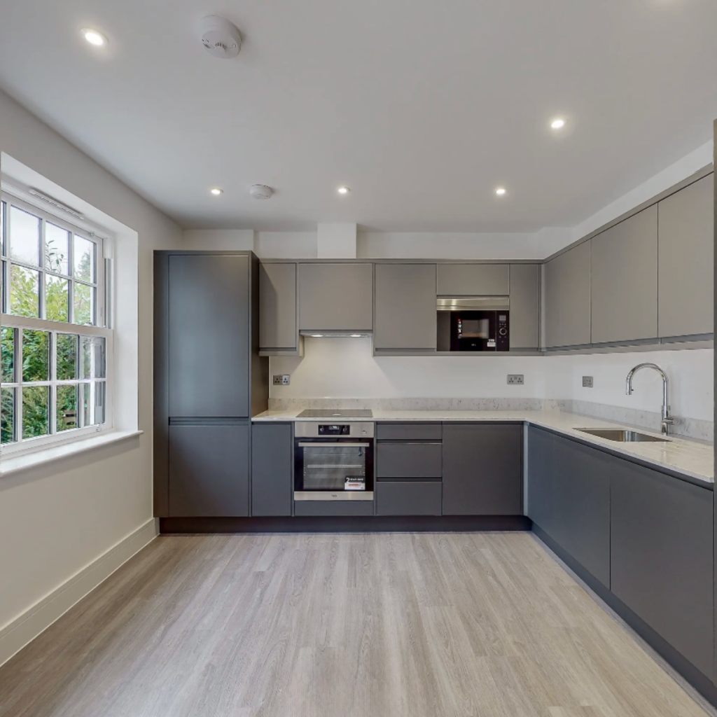 Modern grey L-shaped kitchen with handleless units, white worktops and integrated appliances