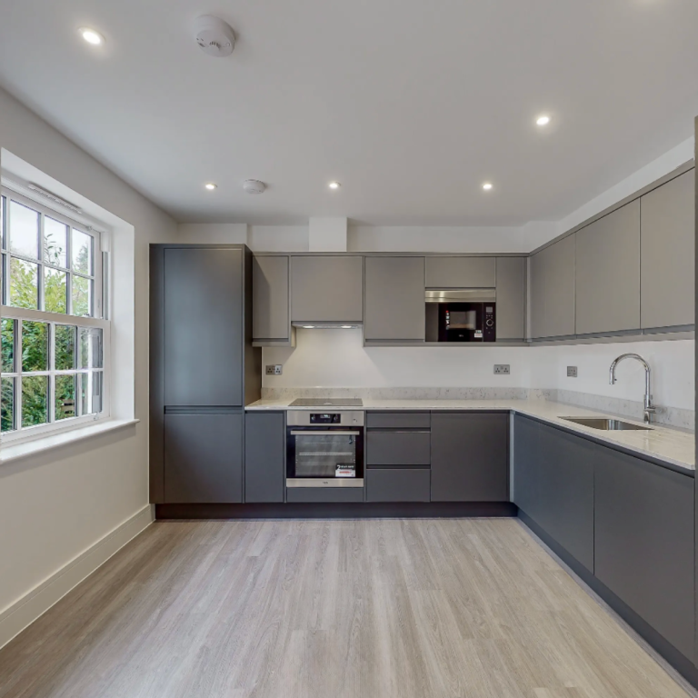 Dark grey handleless kitchen with stone worktop and L-shaped layout in a modern apartment