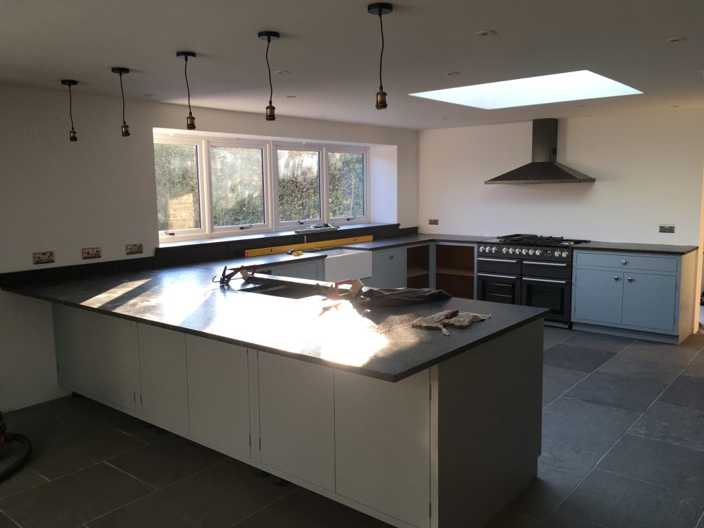 Kitchen extension mid-installation with white cabinetry, granite worktop and skylight over range cooker