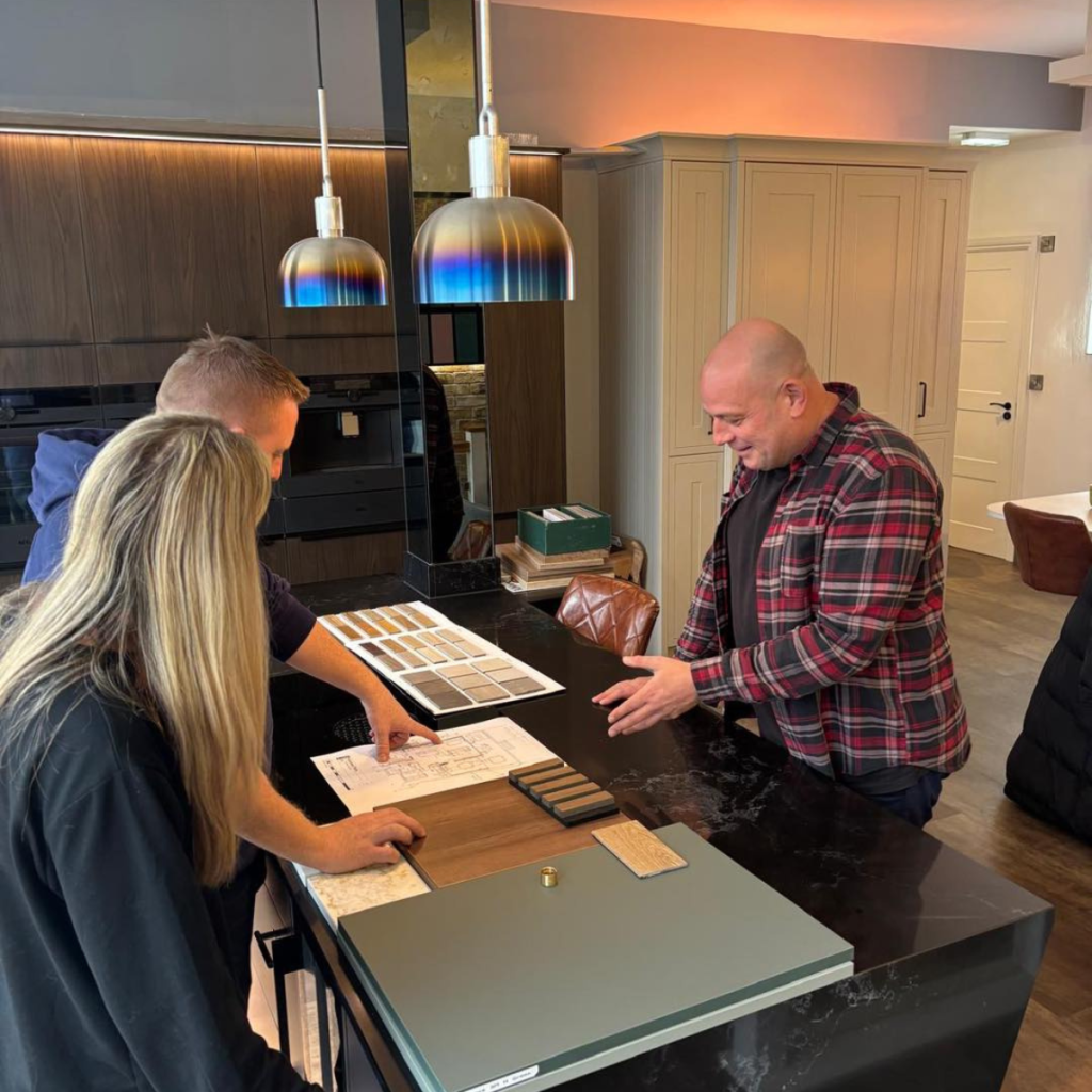 Kitchen designer discussing worktop samples and floor plans with a couple at the Lime Designs showroom